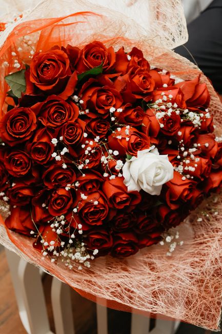 A large bouquet of fresh, vibrant red roses arranged in a dense cluster, accented with delicate white baby's breath flowers. The roses have velvety petals and are tightly packed, creating a lush and f